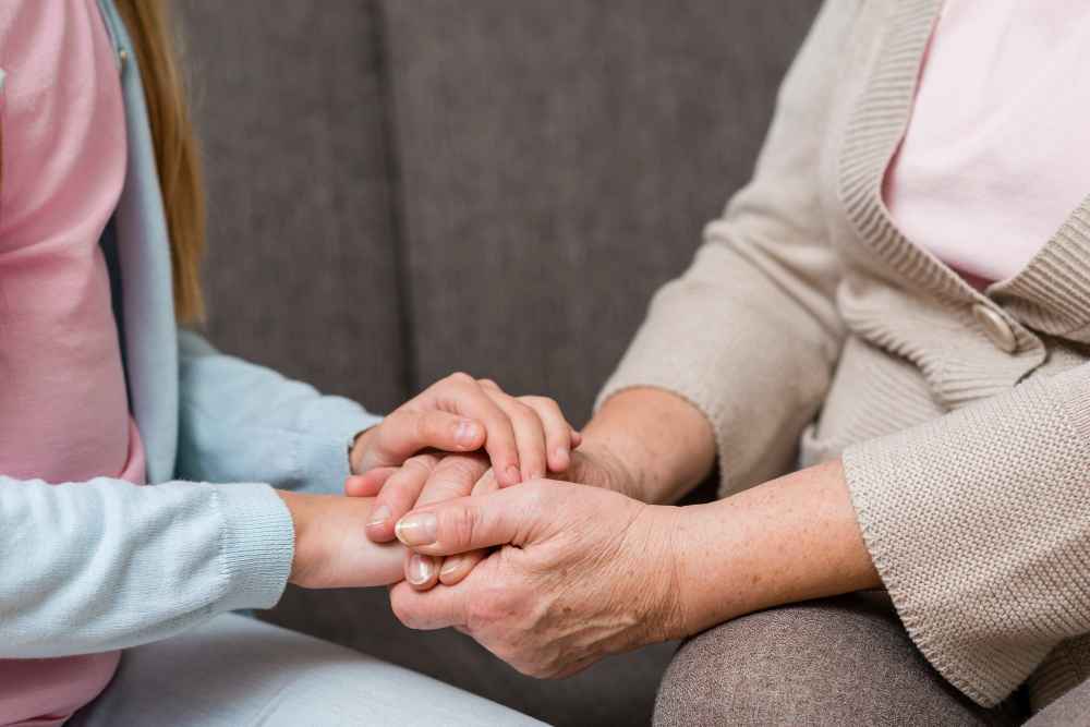 Auxiliaire de vie tenant chaleureusement les mains d'une personne âgée, illustrant l'accompagnement social et relationnel à domicile proposé par Jadis.